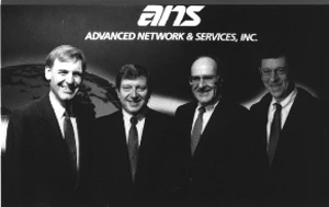 Four men in suits standing together for a photograph in front of a backdrop reading ans, Advanced Network & Services, Inc.