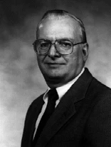 Black and white studio portrait of Eric Aupperle, in glasses, a dark suit and tie.