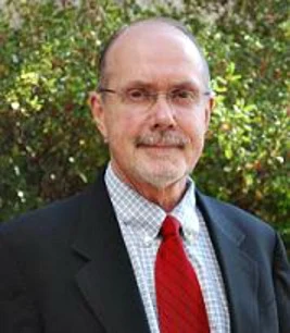 George Strawn outdoors in front of foliage, in a dark jacket, checked shirt and red tie.