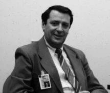 Jack Drescher seated at a desk in a jacket and tie, wearing a visitor's badge.