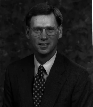 Studio portrait of Larry Bouman in glasses, a dark suit and a patterned tie.